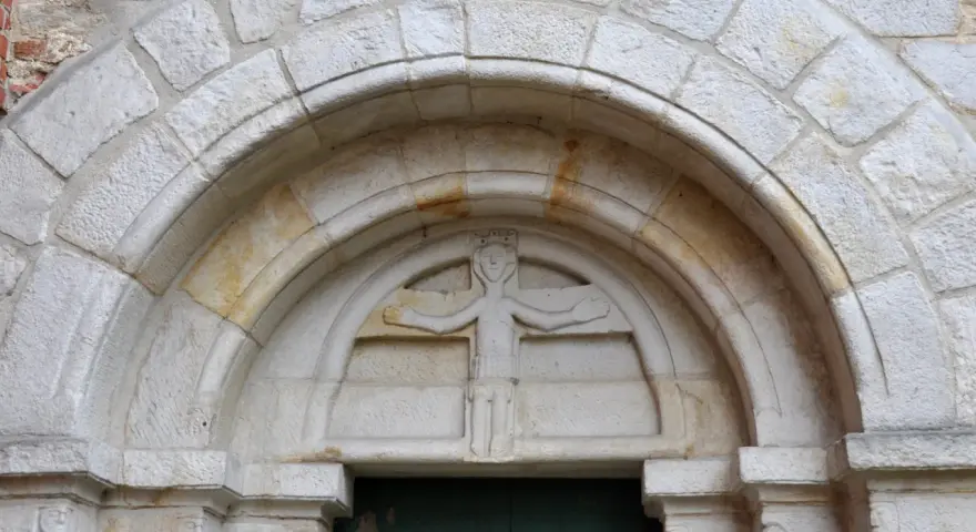 Kamienna płaskorzeźba postaci z koroną nad łukiem portalu, charakterystyczna dla stylu romańskiego.