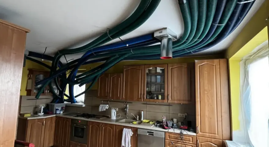 Instalacja rekuperacji w starym domu. W kuchni nad szafkami sufitowymi biegnie gęsta plątanina zielonych i niebieskich rur wentylacyjnych.