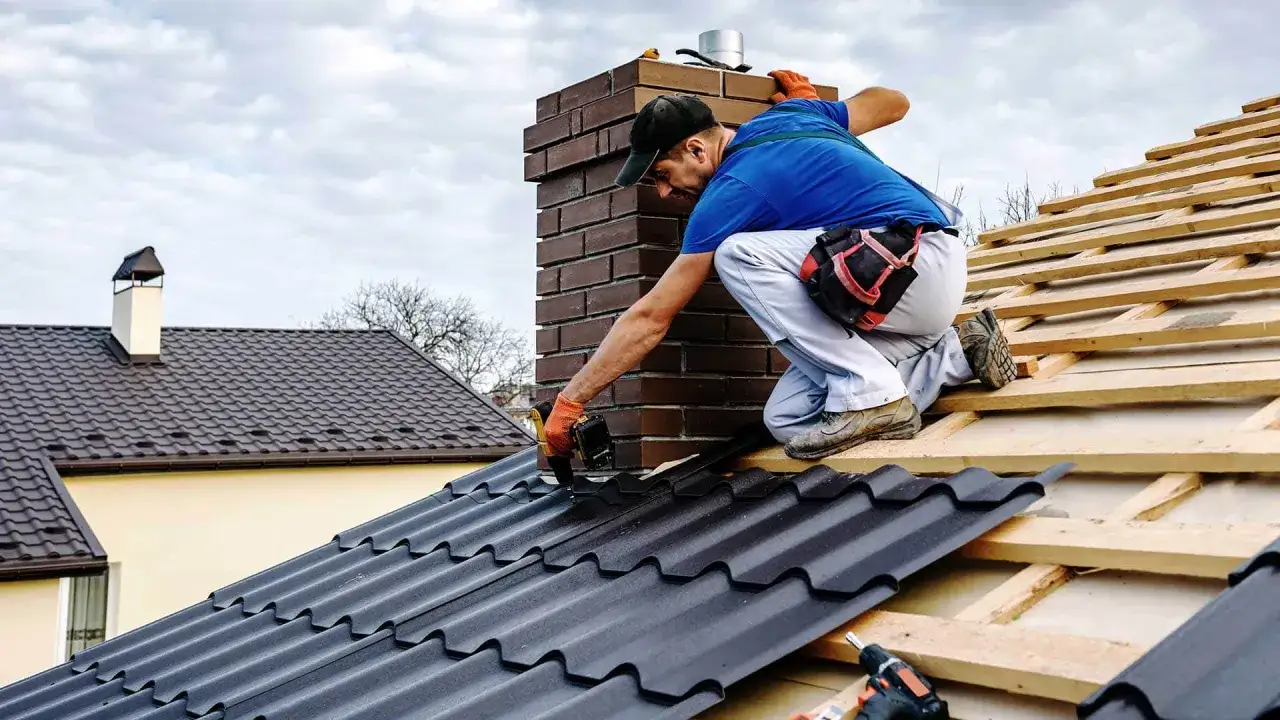 Dekarz montuje dachówkę na dachu dwuspadowym. Szacowany koszt dachu dwuspadowego 100m2 zależy od materiałów.