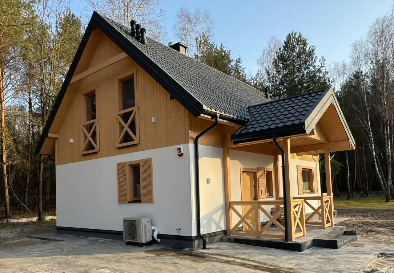 Nowoczesny dom z drewnianymi elementami i werandą, otoczony lasem.