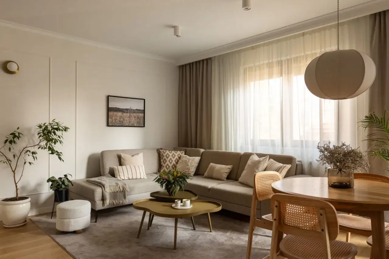 Przytulny salon z sofą w kolorze karmelowym, stolikami kawowymi i okrągłym stołem.
