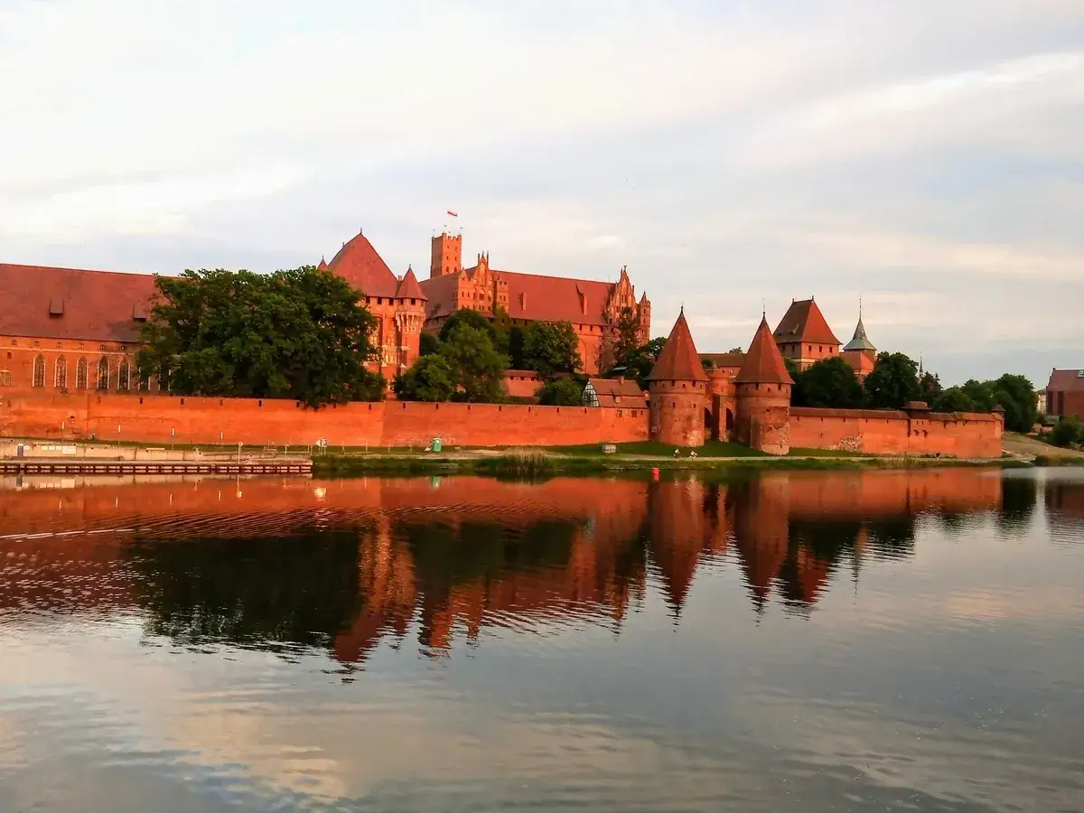 Malbork, największy zamek na świecie, odbija się w spokojnej wodzie o zachodzie słońca.
