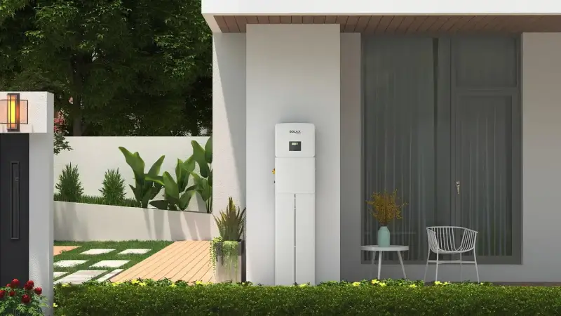 Nowoczesny magazyn energii 5 kW na ile wystarczy? Urządzenie SolaX stoi przy domu z ogrodem, oferując niezależność energetyczną.